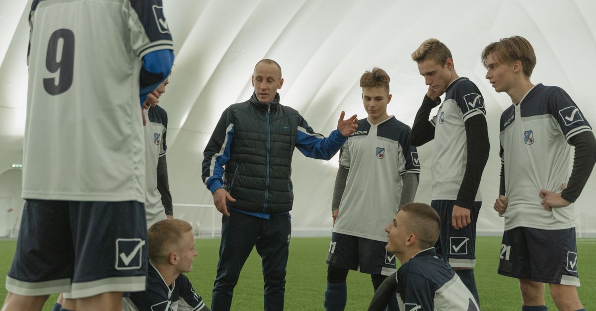 A coach passionately instructs his soccer team during a practice session inside a sports dome.